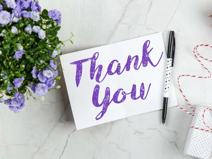 black pen on thank you card on white surface near flower
