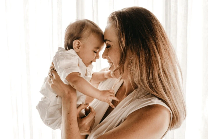 A smiling woman in a white dress carrying her baby