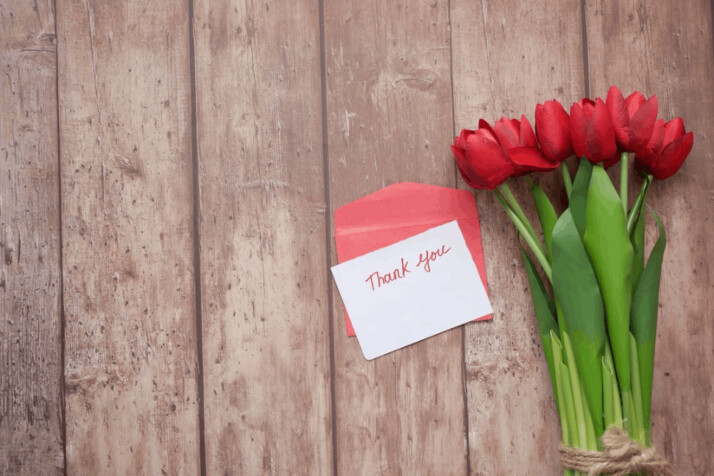 red tulips and thank you card on brown wooden table