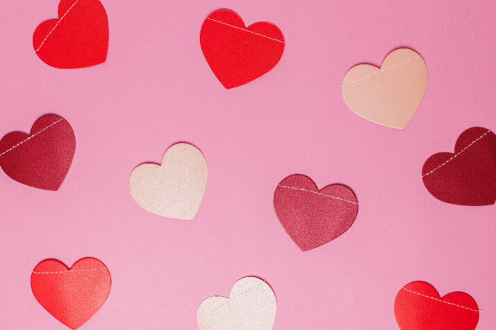 Several heart cut outs placed all over a pink surface.