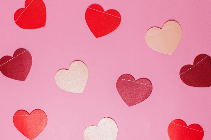 Several heart cut outs placed all over a pink surface.