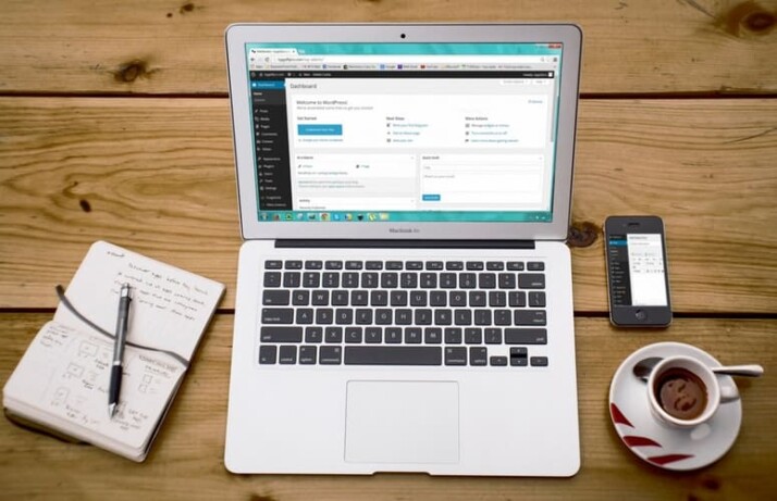 laptop, tea cup, mobile phone and jotter on brown table