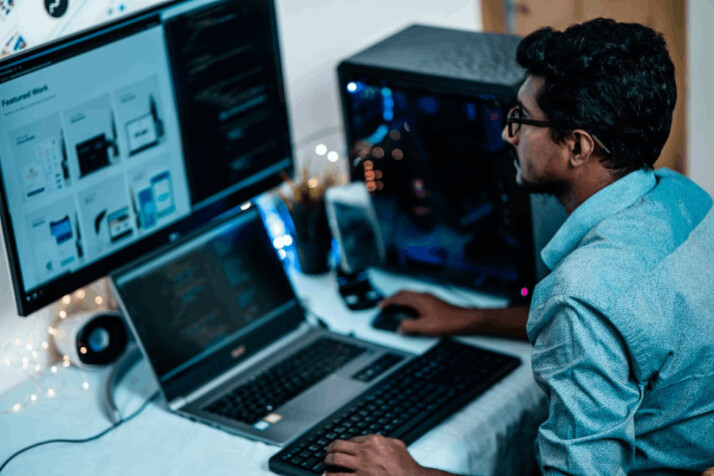 man with curly hair in blue shirt and glasses using computer