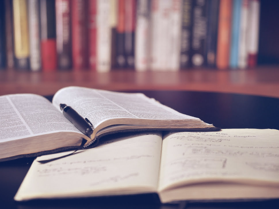 A notebook and an open book with a pen on its pages.