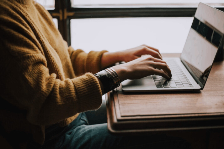 Person sitting in front of a laptop computer placed on a wooden table