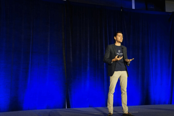 men wearing black blazer speaking to a crowd with blue background