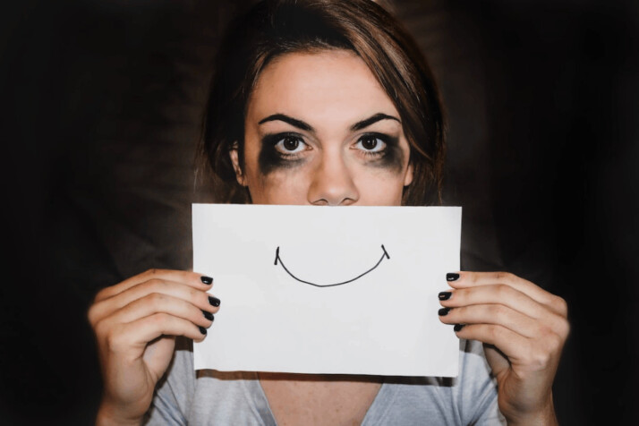 person holding white printer paper with a smiley face over their lips.