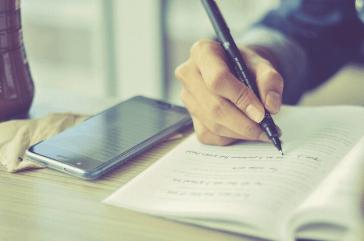a person holding a pen and writing on a notepad.