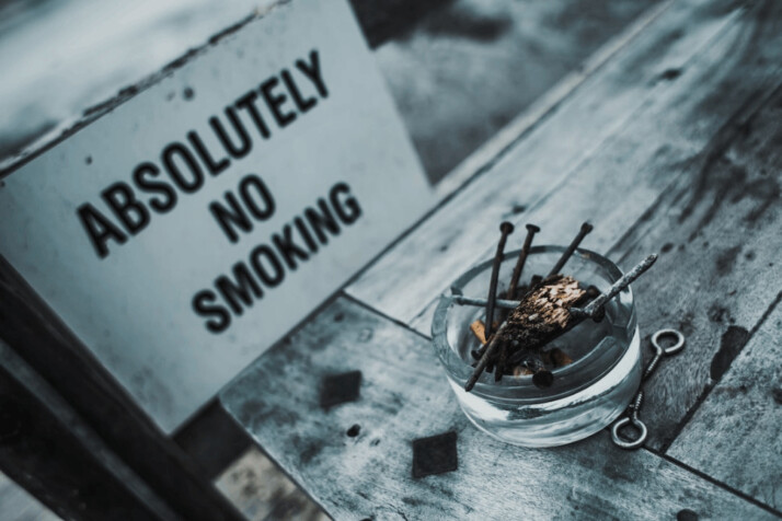 A clear glass ashtray with a board Absolutely No Smoking