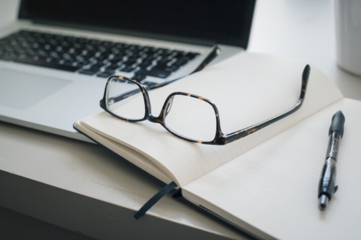 An open notebook with glasses and a pen on top of it.