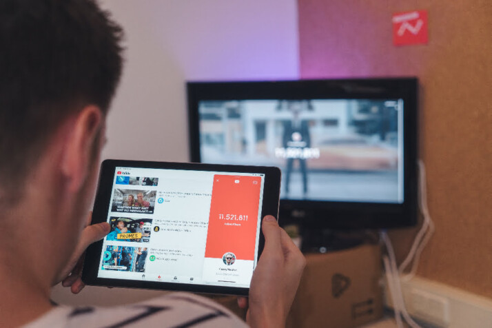 A guy exploring YouTube videos using a tablet with a monitor in the back.