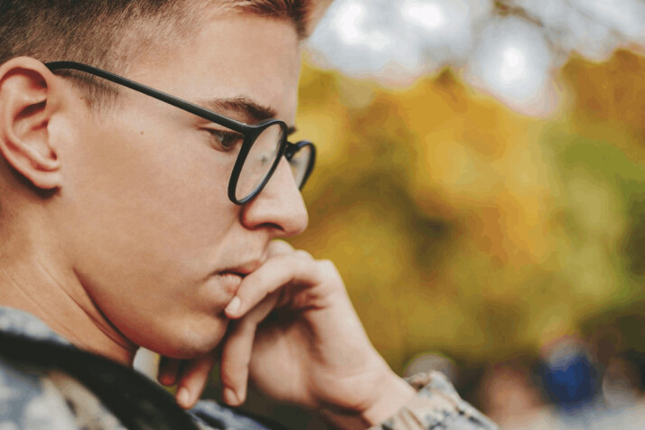 boy with black framed eyeglasses holding face in a discerning manner.