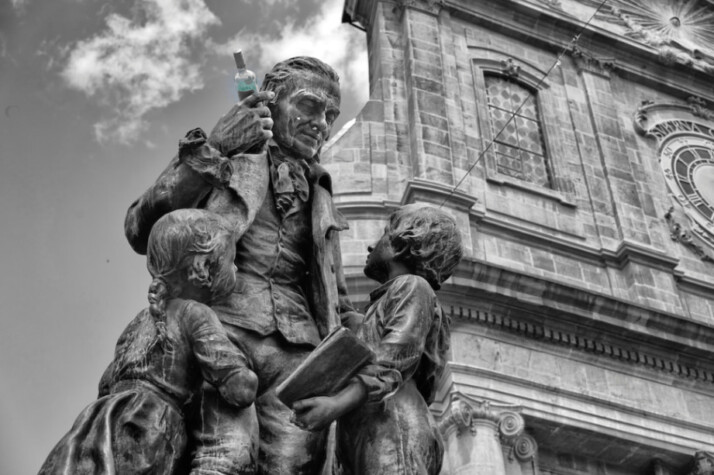 man holding bottle near two children statue photo in black and white.