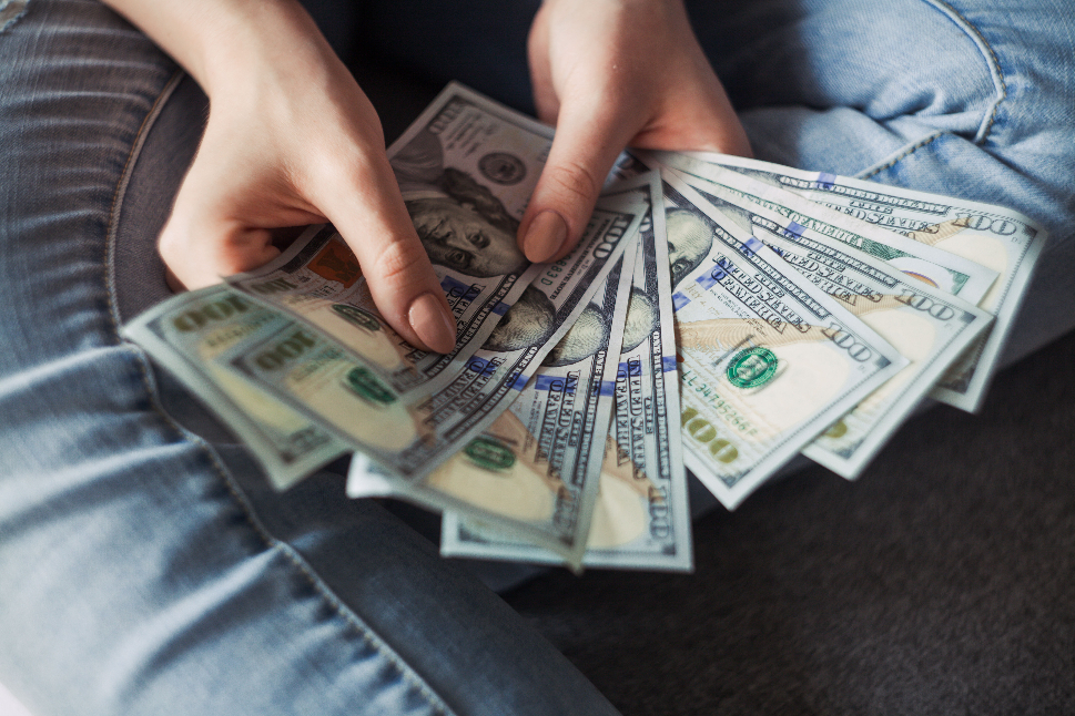 a woman wearing jeans holding 9 100 US dollar bills.