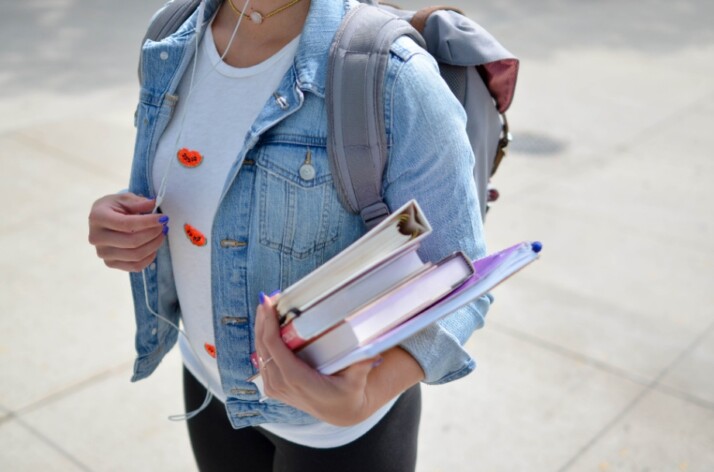 A student wearing a jean jacket and holding a bunch of books on one hand.