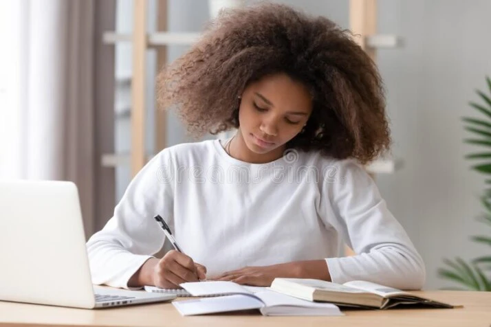 young girl waring white sweater writing with pen on book