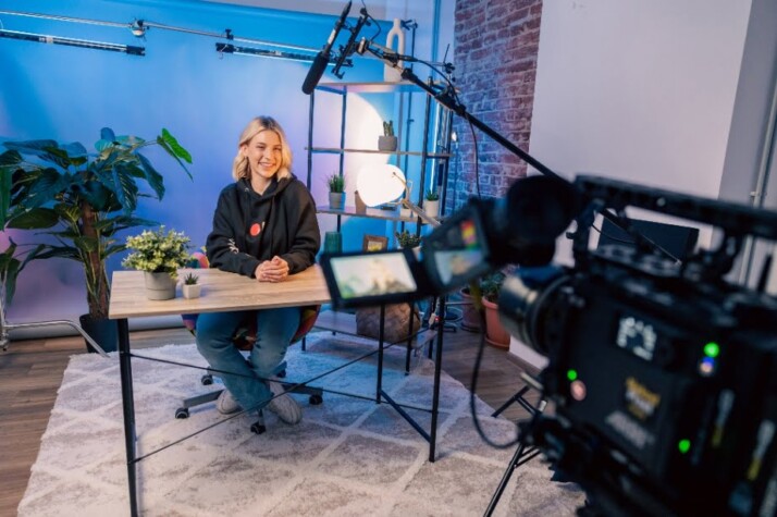 A filming studio with a woman smiling at the camera.