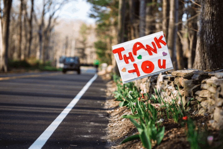 white sign on the side of the forest road that reads thank you