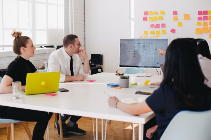 A group of people sitting around a table discussing something on the computer screen.