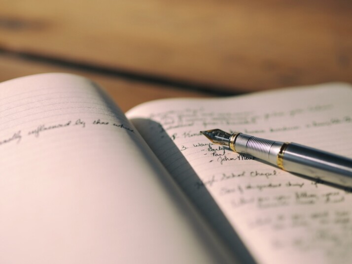 An open notebook with a fountain pen placed on the pages.