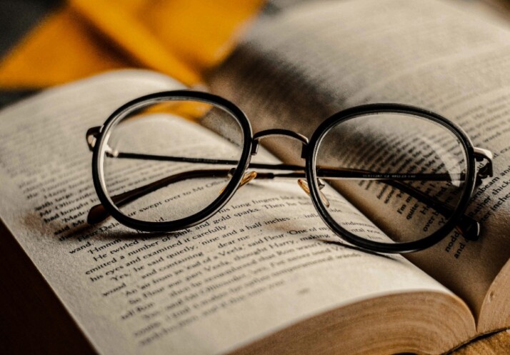 A pair of reading glasses placed on the pages of a thick book.