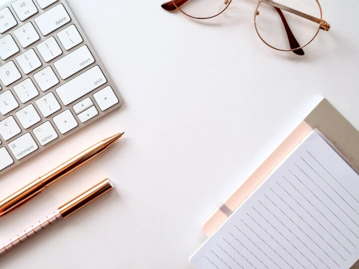 A keyboard placed next to a notebook and some glasses.