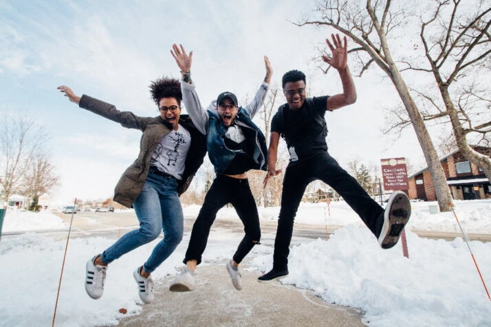 Three friends smiling in the middle of a jump with a snowy background.