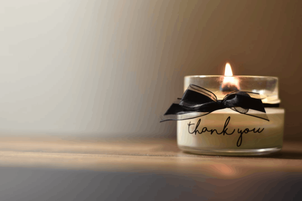 A glass candle holder with a black ribbon and thank you text