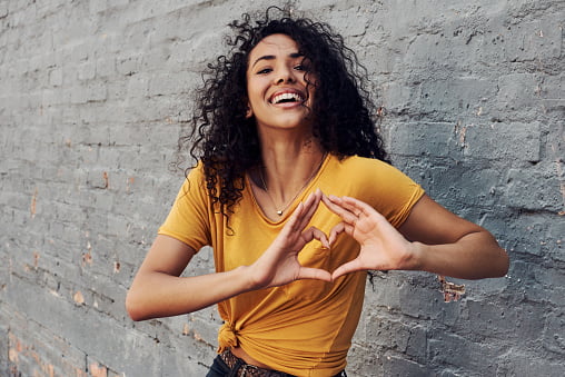 woman wearing yellow shirt making a love sign with both hands