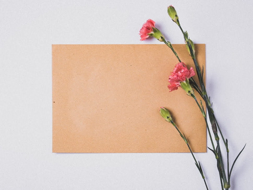 A blank brown card next to some pink flowers.