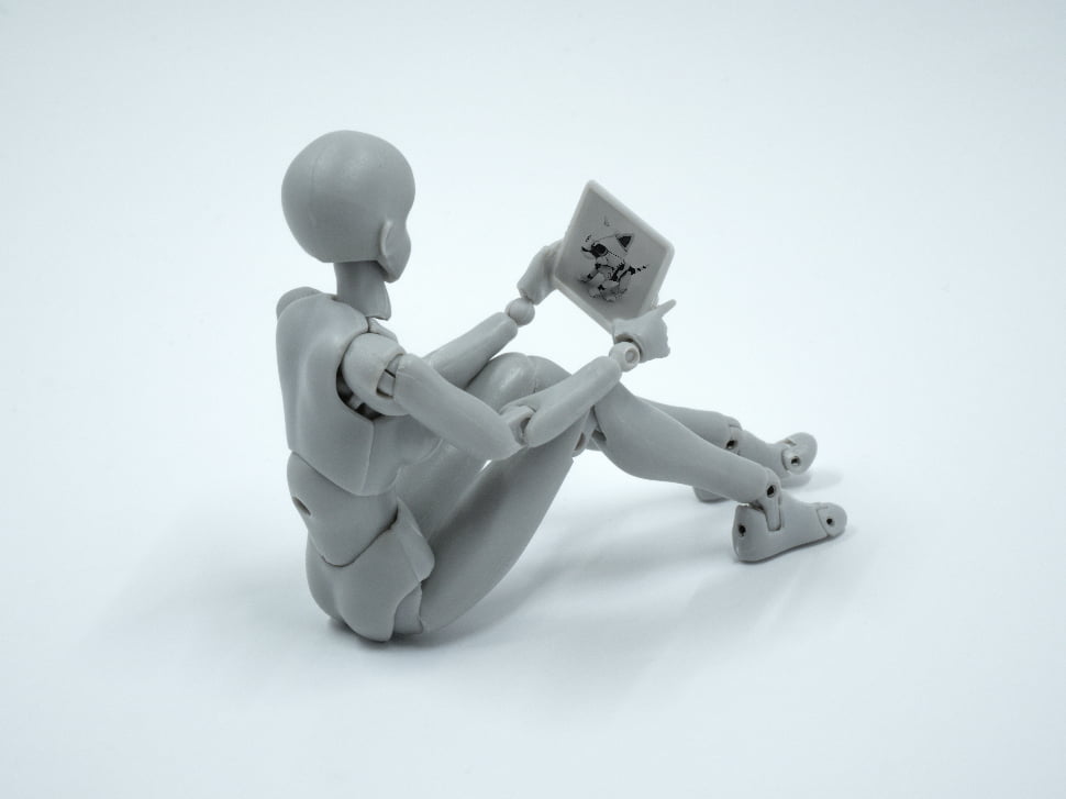 A plain and grey doll representing a person watching something on an iPad.