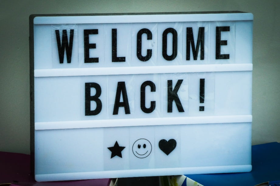 A welcome back sign with emojis on a white surface.