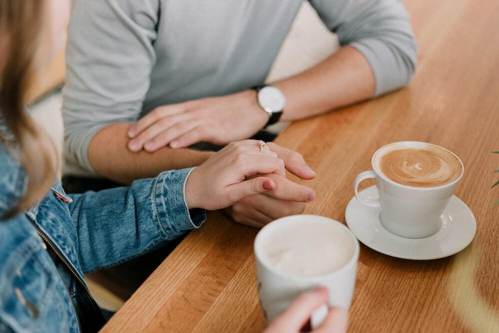 A man and woman holding hands while drinking coffee. 