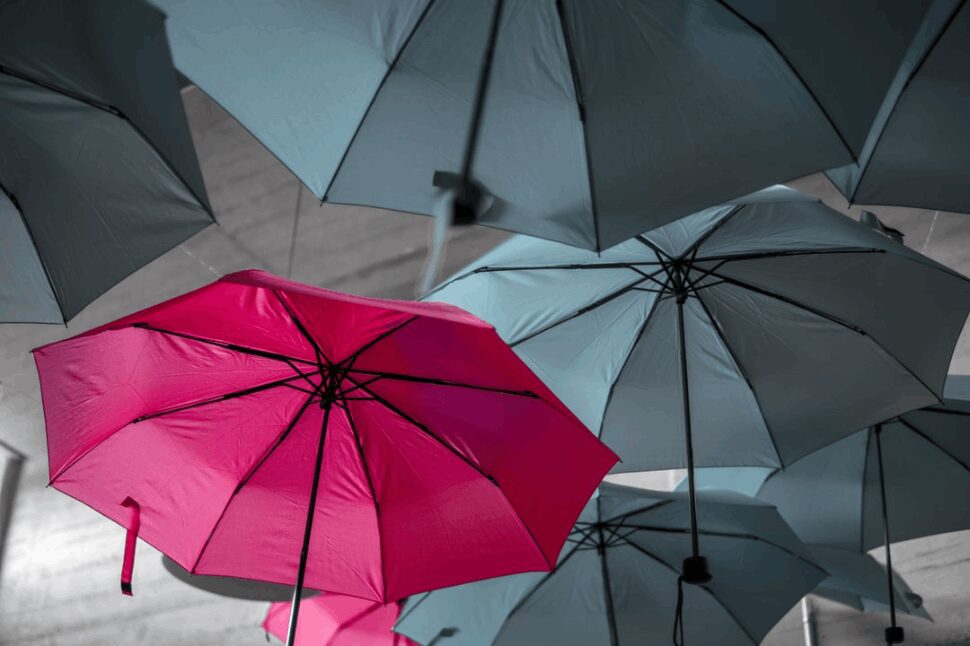 A pink umbrella that stands out from a group of grey umbrellas.