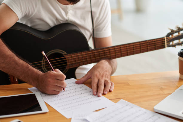 person wearing white shirt holding guitar and writing with pencil on white paper