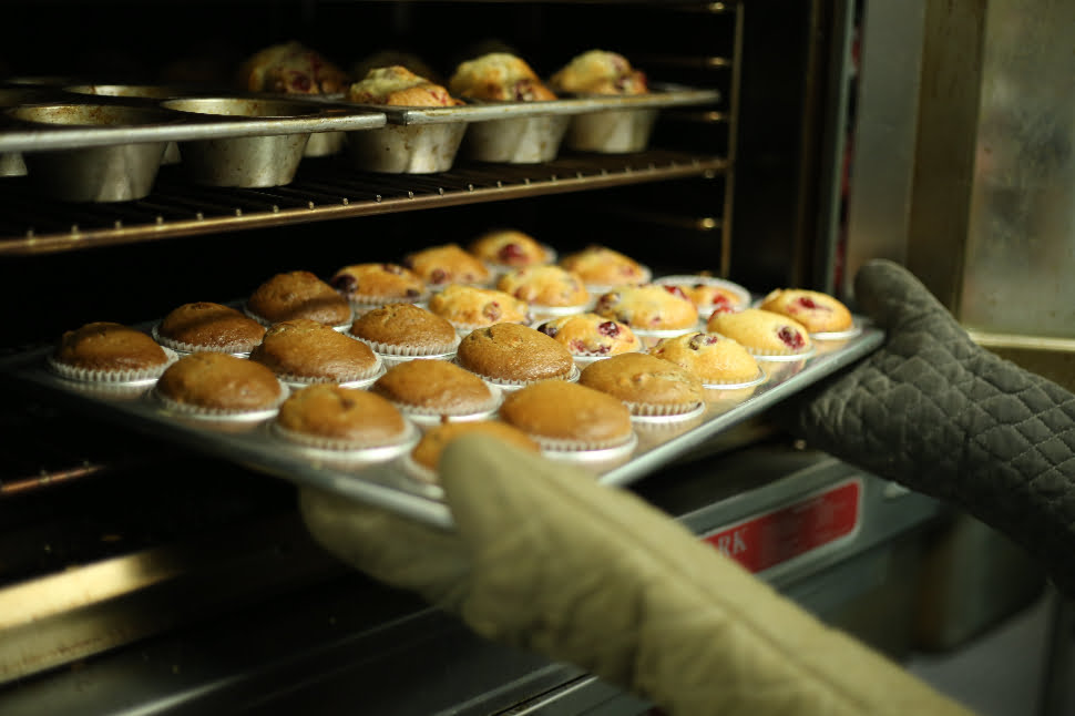 A fresh batch of muffins being taken out of an oven.