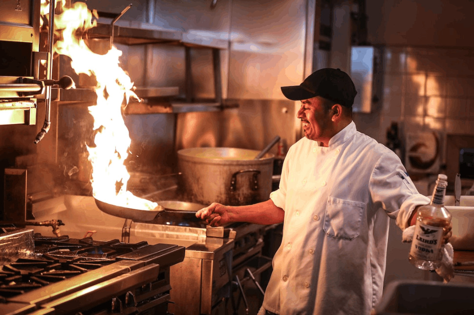 man in white chef uniform cooking pouring vodka on pan