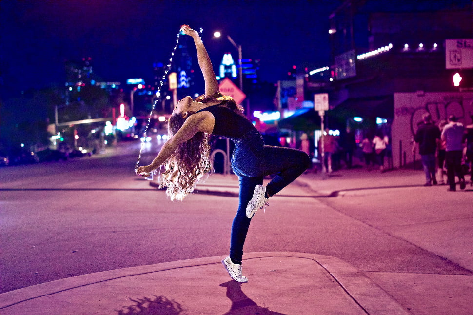 A woman gracefully dancing in the streets while holding a string of lights.