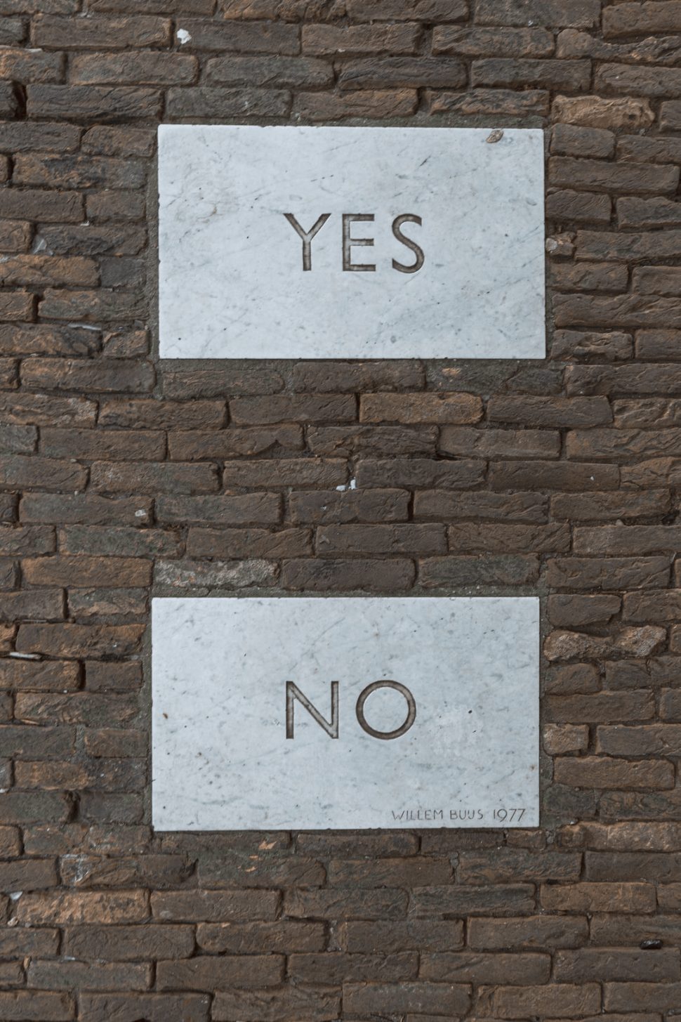 a brick wall with two signs, one saying yes and the other no.