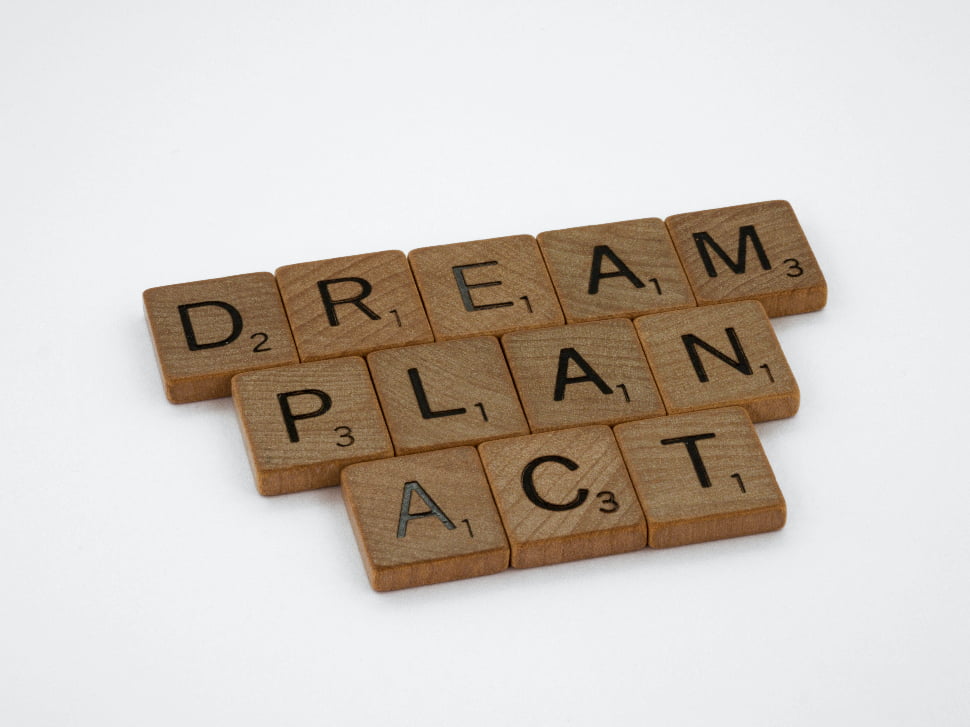 DREAM PLAN ACT wooden scrabble blocks on a white surface. 