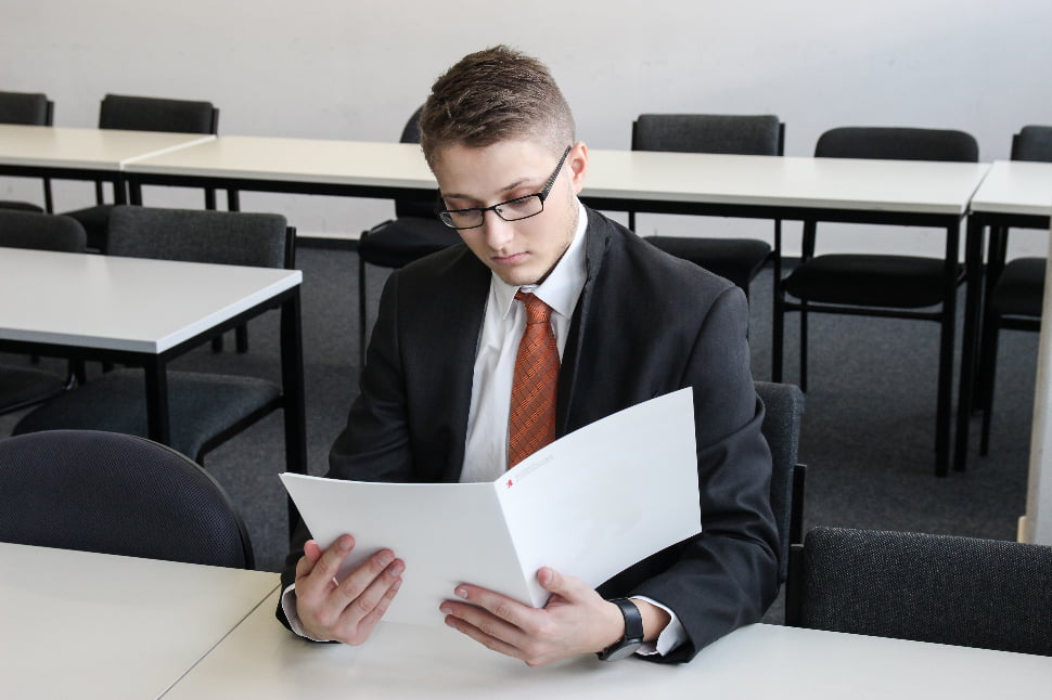 A guy in a suit reading something in a white folder.