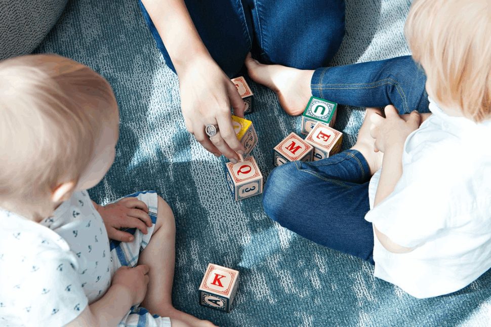 two toddlers playing with letter cubes sitting on the ground