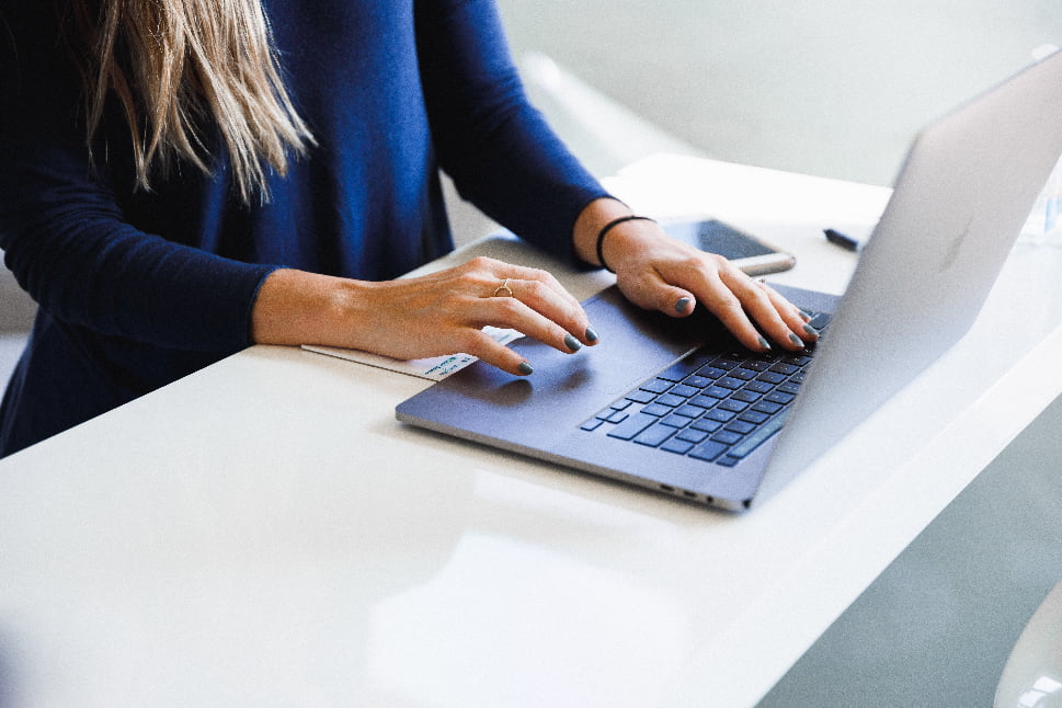 A woman wearing a blue sweater typing something on her MacBook.