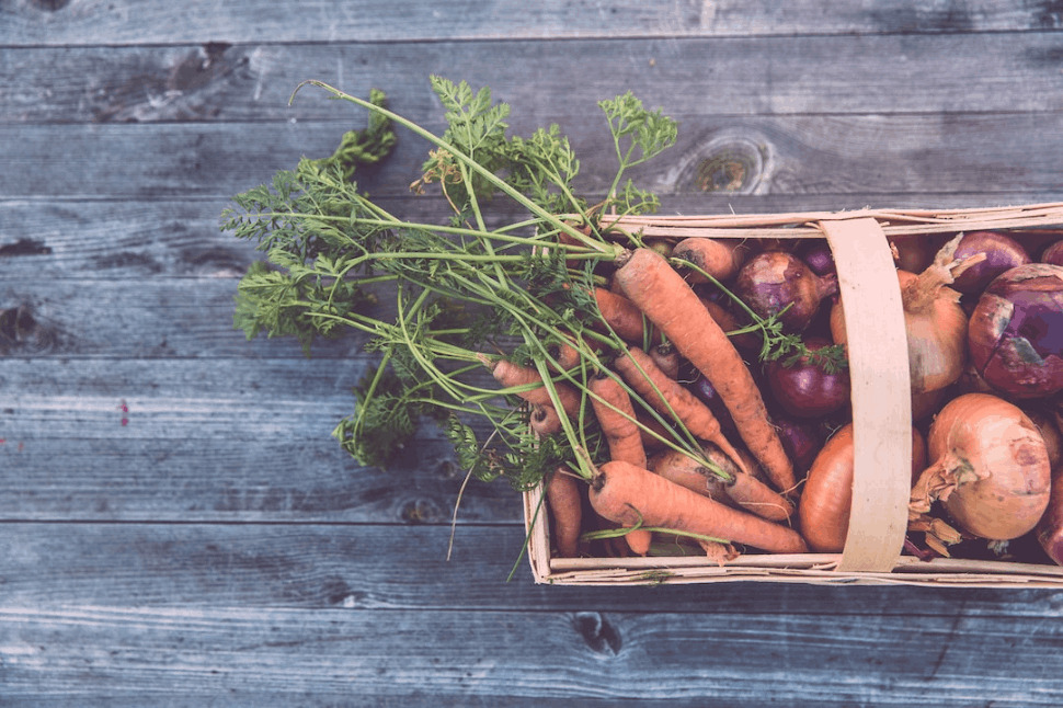 carrots and onions in brown wicker basket on wooden table