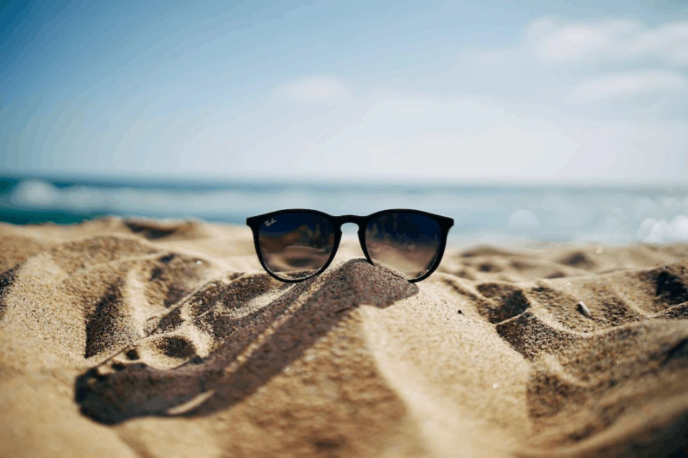 A black Ray-Ban Wayfarer sunglasses placed on beach sand