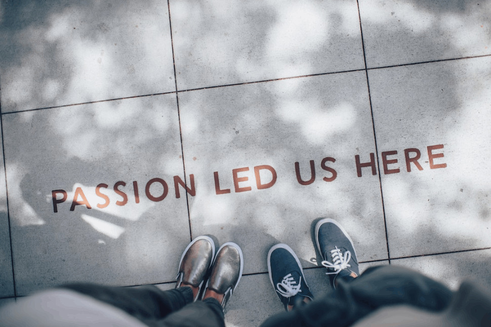 two person standing on gray tile paving that says Passion Led Us Here. 