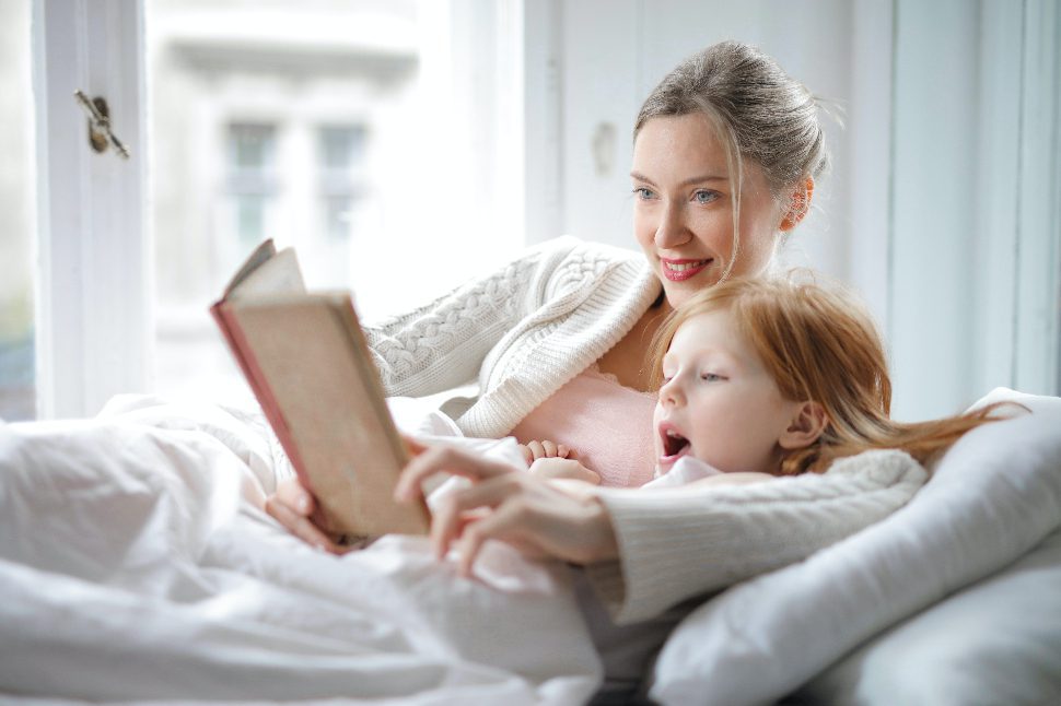 A woman and her daughter laying in bed having fun reading a book.