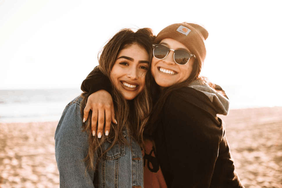 a woman hugging other woman while smiling at beach