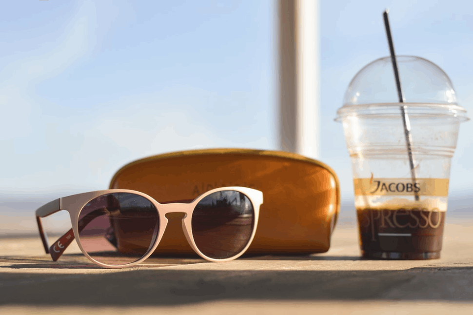 selective focus photography of white sunglass near brown leather pouch and clear Jacobs Espresso cup