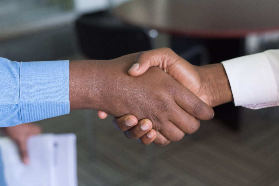 two black man wearing shirts shaking hands in an office.
